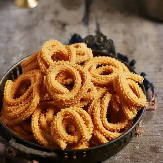 A close-up of freshly made mullu murukku, a traditional South Indian snack, arranged in a spiral shape. The golden-brown, crispy snack has a textured surface, with its intricate ridges showing the signature pattern. The murukku looks crunchy and inviting, placed on a traditional plate, enhancing its cultural significance.