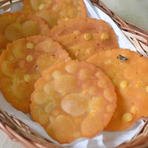 A close-up of crispy, golden-brown thattai, a traditional South Indian snack, arranged in a stack. Each thattai is round, thin, and has a slightly rough surface with visible cracks, indicating its crunchy texture. Made from rice flour and seasoned with spices, the snack is deep-fried to perfection, giving it a light, crispy appearance. The thattai looks appetizing and perfect for festive occasions or casual snacking