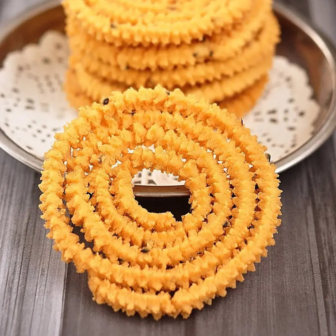 A wide angle of stcked freshly made mullu murukku, a traditional South Indian snack, arranged in a spiral shape. The golden-brown, crispy snack has a textured surface, with its intricate ridges showing the signature pattern. The murukku looks crunchy and inviting, placed on a traditional plate, enhancing its cultural significance.